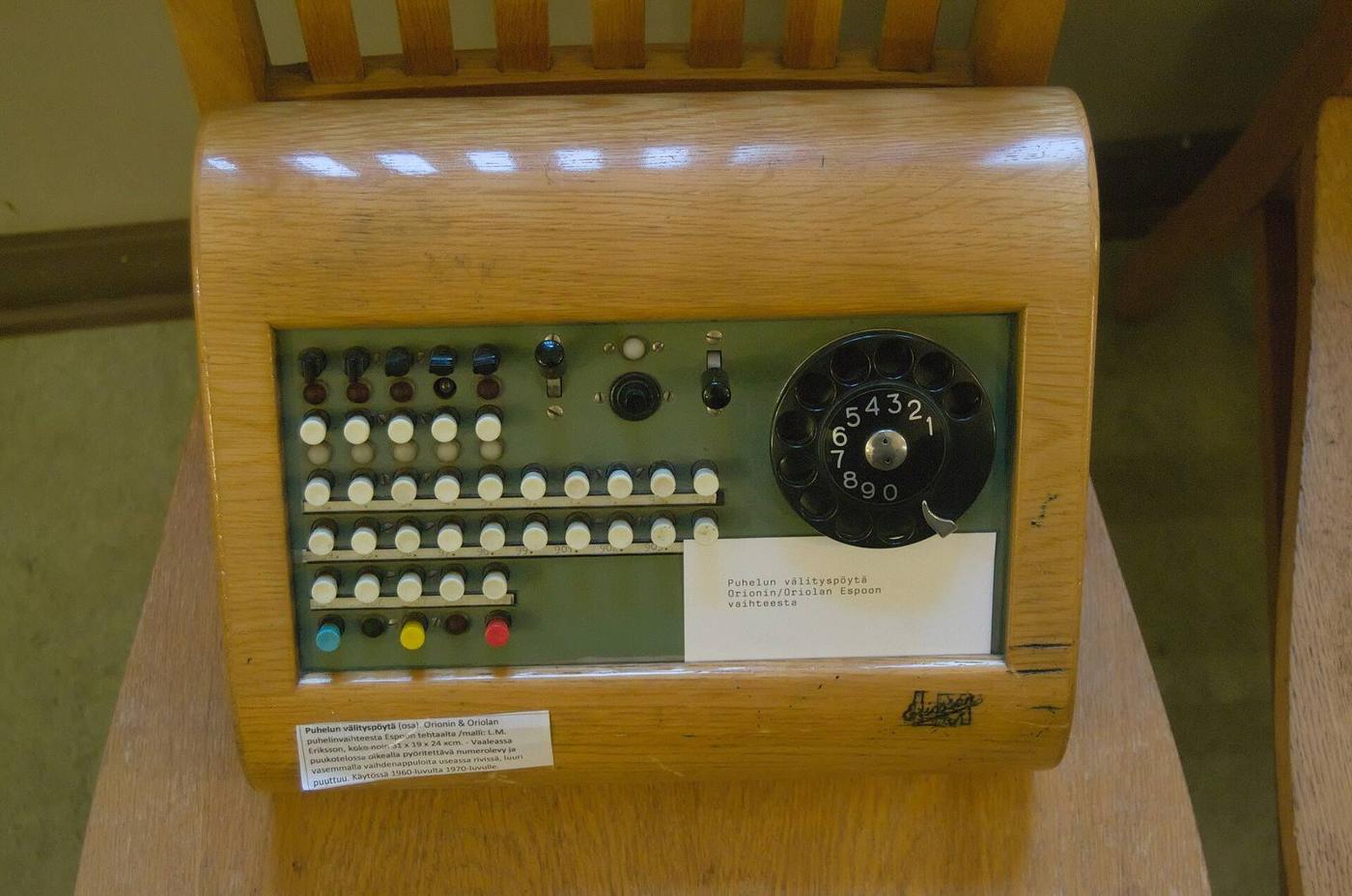 A wooden switchboard with rows of white and coloured keys and a rotary dial.